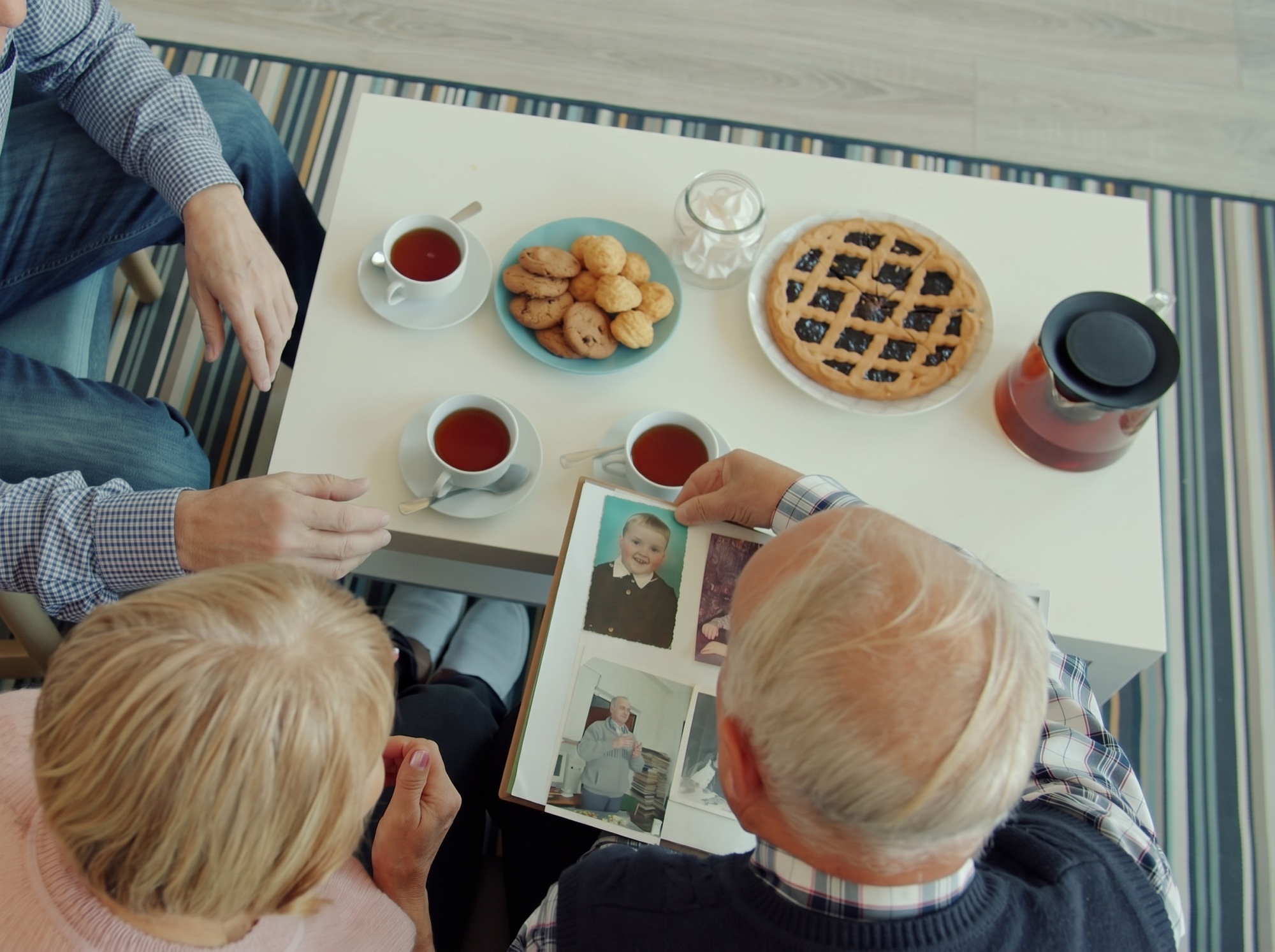 A couple looking through a family photo album together over tea, with a relative seated beside them